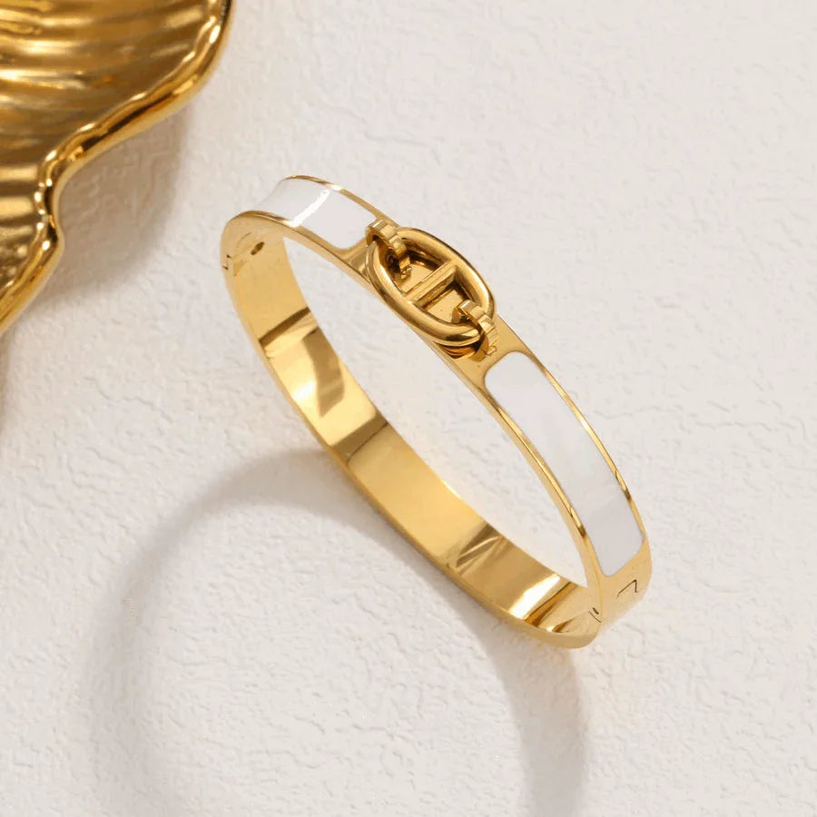 Gold and white enamel clasp bracelet on textured beige surface